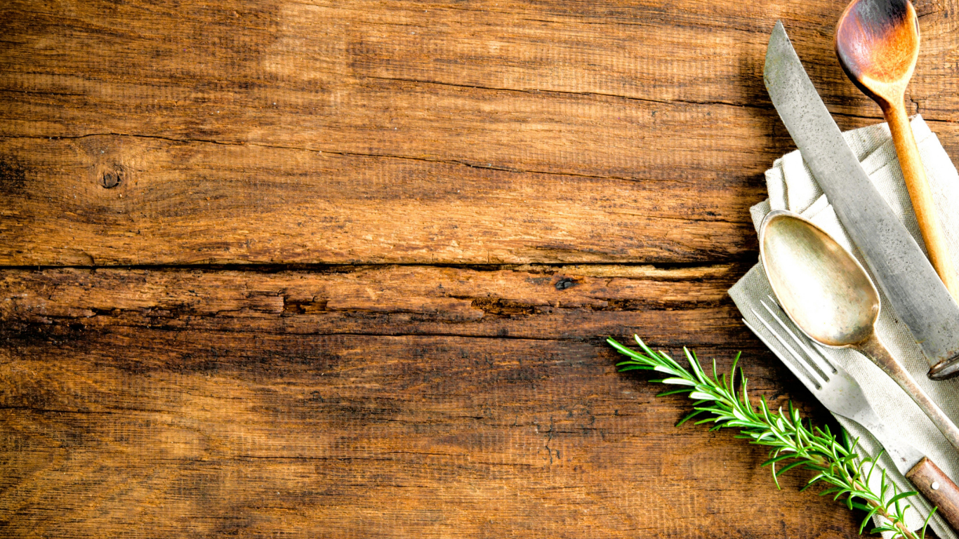 Wooden table with cutlery and a sprig of rosemary
