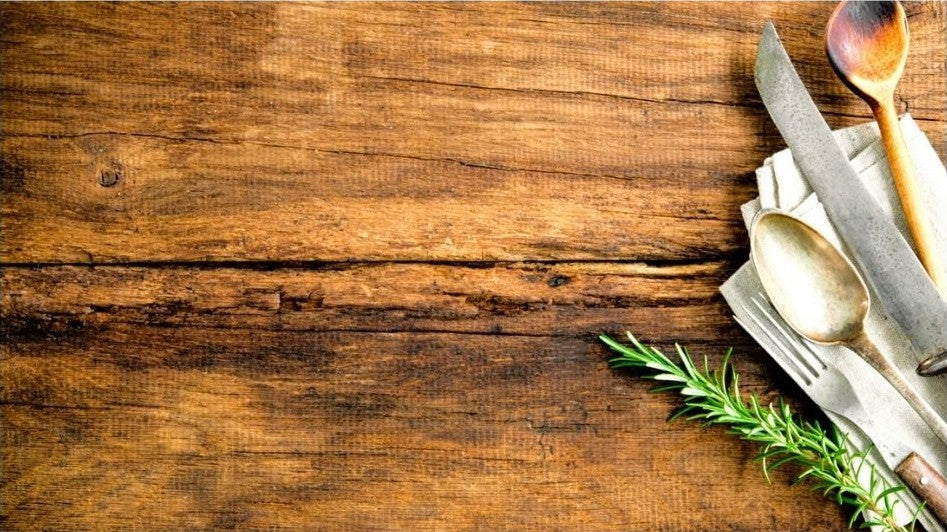 A wooden table with rustic silverware and a sprig of rosemary.